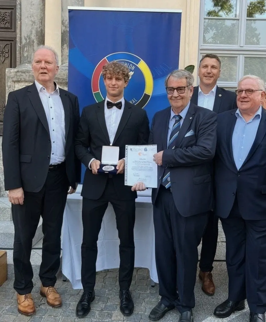 Jakob Rosenberger im Smoking mit der Pierre de Coubertin-Medaille im Etui, daneben Hugo Schuster mit der Urkunde, im Hintergrund die Panathlon-International-Beachflag